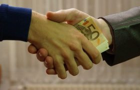 Nærbillede af to mennesker som giver hånd. I den ene hånd er der pengesedler.