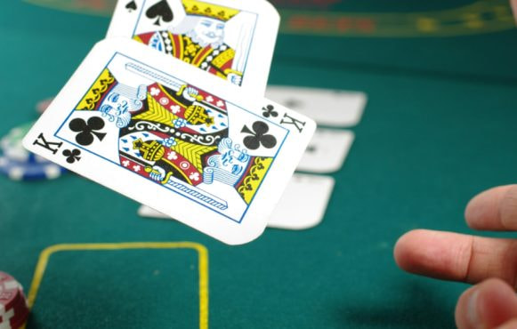 Kort kastes på et pokerbord med chips og andre kort synlige i baggrunden