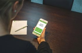 Kvinde ved bord med mobil og opgaver.