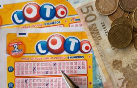 Un biglietto del lotto con numeri spuntati, una penna e soldi su un tavolo.