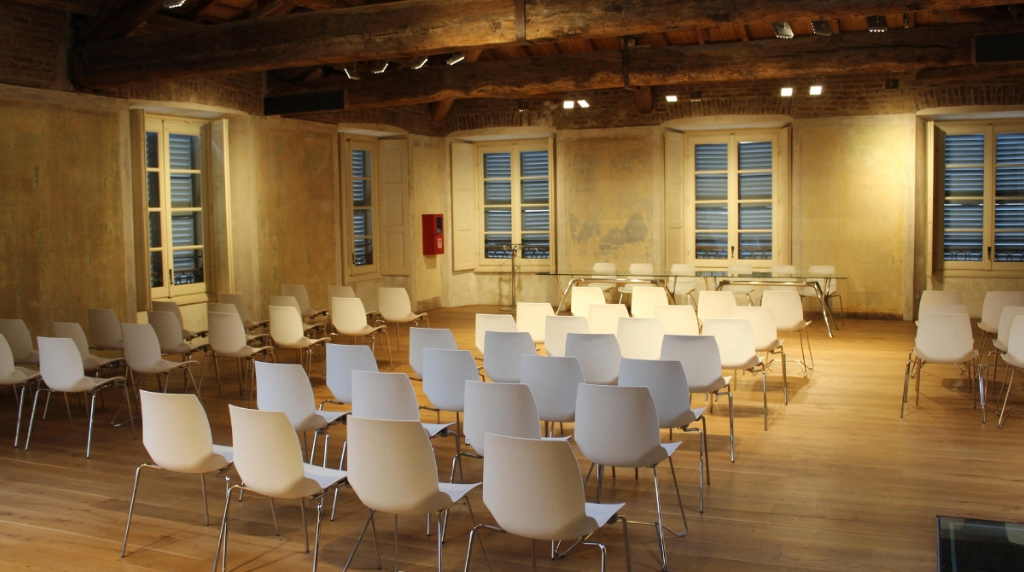 Sala conferenze vuota con sedie bianche e travi a vista.