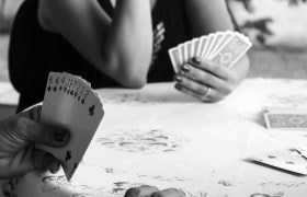 Persone che giocano a carte attorno a un tavolo, dettaglio delle mani e delle carte in bianco e nero