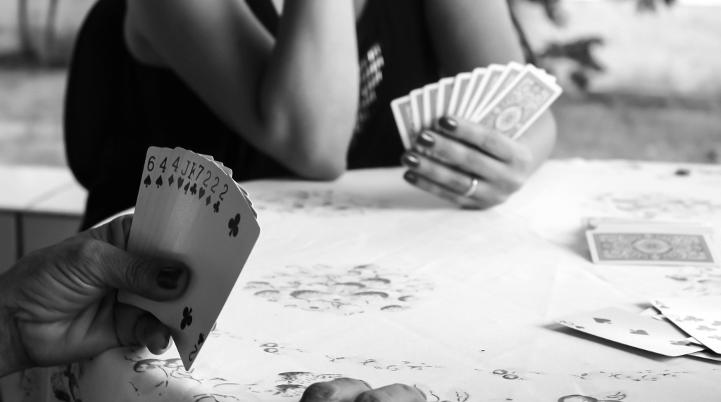 Persone che giocano a carte attorno a un tavolo, dettaglio delle mani e delle carte in bianco e nero