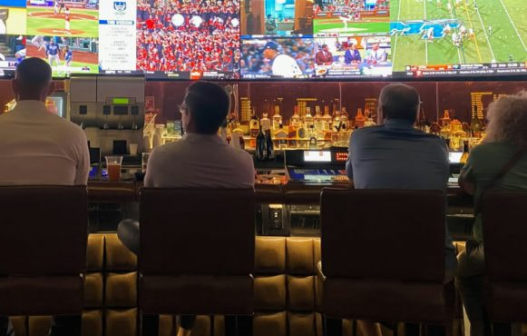 Persone sedute al bancone guardano partite su maxi schermo sportivo