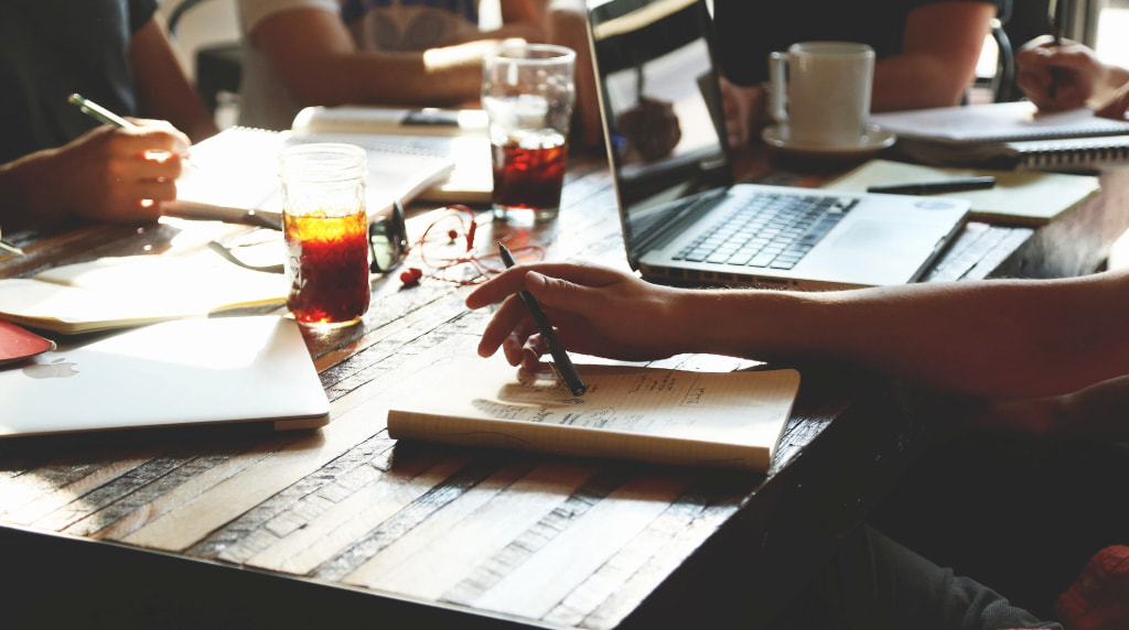Persone al lavoro con laptop, taccuini e bevande.