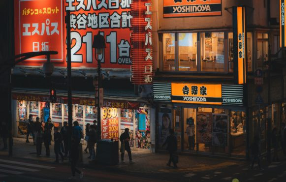 Strada giapponese con insegne luminose, locali affollati e passanti notturni.