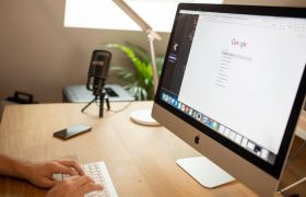 Postazione di lavoro con iMac acceso e mani sulla tastiera.