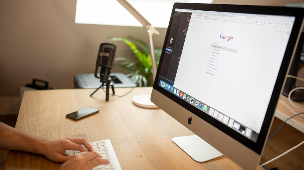 Postazione di lavoro con iMac acceso e mani sulla tastiera.