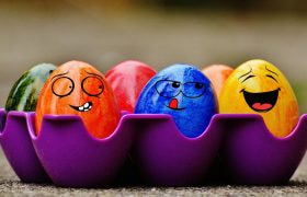 Uova di Pasqua colorate con facce sorridenti in portauova viola.