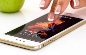 Mano usa smartphone con schermo acceso su tavolo bianco