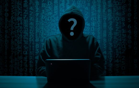 Figura incappucciata davanti al laptop tra codici digitali