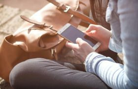 Jonge vrouw zittend op de grond, met in haar handen een smartphone