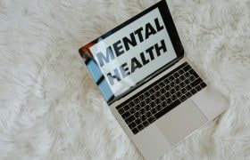 Laptop op wit wollig kleed en op het scherm staat in zwarte letters de tekst “mental health”
