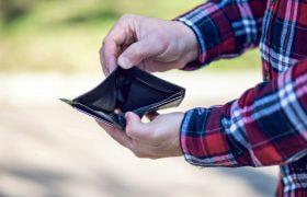 Armen van een man met een geruite blouse, die een lege portemonnee laat zien.