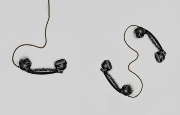 Drie oude zwarte telefoon-hoorns met snoer, op een grijze achtergrond