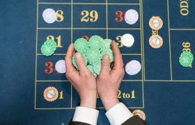 Twee handen die veel fiches vasthouden boven een blauwe roulettetafel