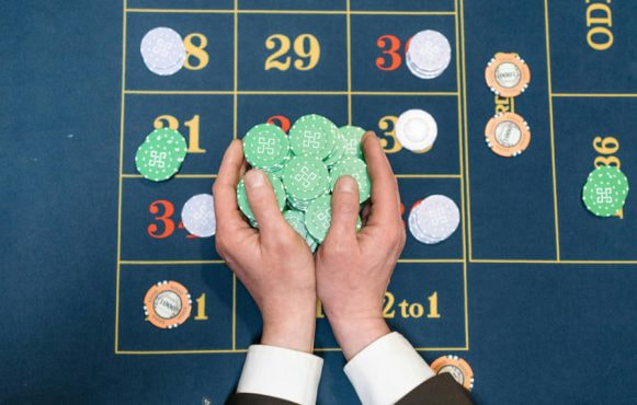 Twee handen die veel fiches vasthouden boven een blauwe roulettetafel