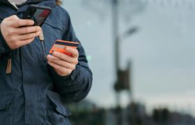 Jongeman met in de ene hand zijn smartphone en in de andere zijn betaalpas