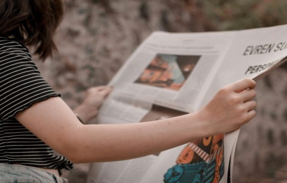 Vrouw leest een krant in de buitenlucht.