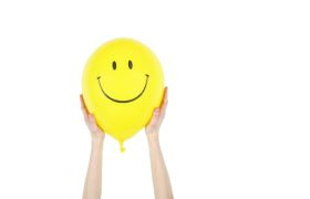 Handen die een gele ballon met lachende smiley vasthouden