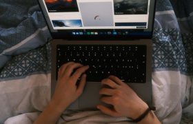 Twee kinderhanden die laptop vasthouden en parachutelanding bekijken vanuit bed.