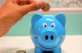 Blauw lachend spaarvarken en hand met een euromunt