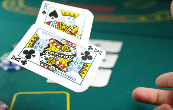 Groene tafel en een hand die twee kaarten (koningen) opgooit