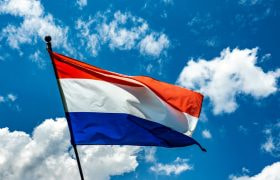 Nederlandse vlag die wappert tegen een blauwe lucht met schaapjeswolken