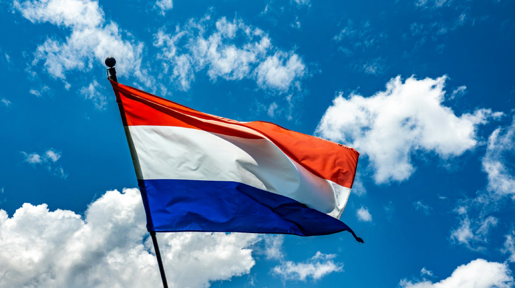 Nederlandse vlag die wappert tegen een blauwe lucht met schaapjeswolken