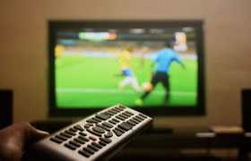 Televisie met voetbalwedstrijd en een hand die afstandsbediening vasthoudt