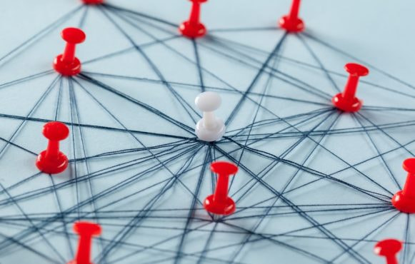 Prikbord met meerdere rode en een witte punaise, verbonden met touwtjes