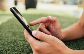 Handen van iemand die smartphone vasthoudt, buiten op het gras