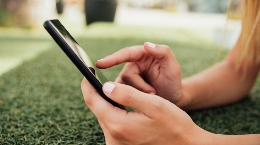 Handen van iemand die smartphone vasthoudt, buiten op het gras