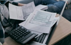 Man op bank met papieren, een rekenmachine en laptop