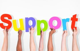 Zeven armen, waarvan iedere hand een gekleurde letter vasthoudt van het woord “support”