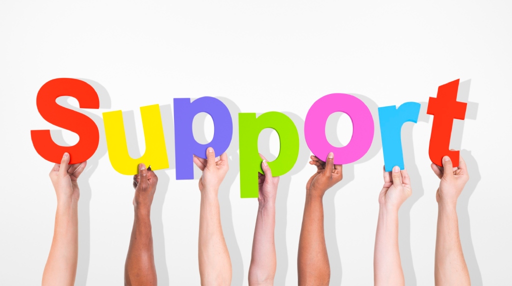 Zeven armen, waarvan iedere hand een gekleurde letter vasthoudt van het woord “support”