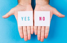 Twee handen met ieder een briefje, op de ene staat Yes en op de andere No