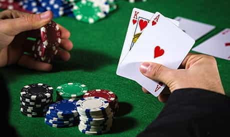 a king of clubs and an ace of clubs in a players hand with casino chips on a green felt table