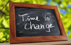 O tablă neagră încadrată într-o ramă de lemn pe care este scris cu cretă albă mesajul „Time to Change”.