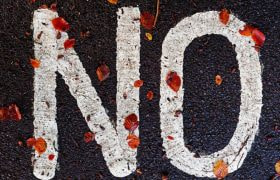 Cuvântul „NO“ scris pe asflat, acoperit de câteva frunze maro