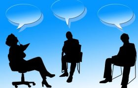 Siluete de trei persoane în dezbatere, cu baloane de dialog și semn de întrebare în centru