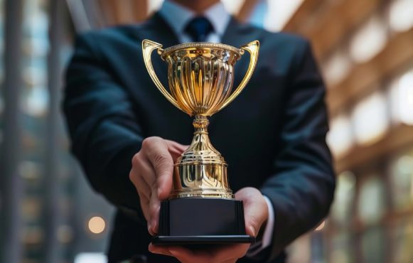 Trofeu auriu ținut în mâinile unei persoane îmbrăcate în costum