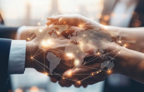 Două persoane strâng mâna, peste imagine fiind suprapusă o hartă digitală a lumii