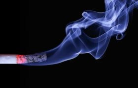 A lit cigarette smoking in front of a black background.