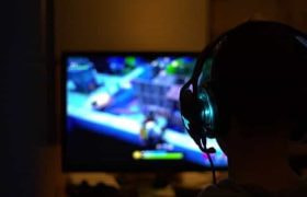 The silhouette of the back of a person while they play a videogame with a headset on.