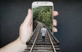 A person holding up a smartphone which has a man walking along train tracks emerging out of it.
