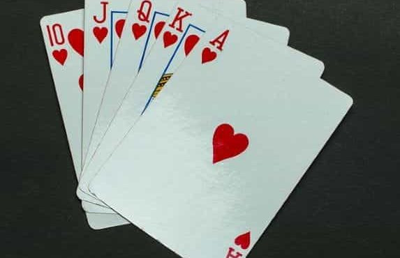 Five playing cards in the same suit of hearts lying flat on a grey surface.