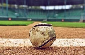 A worn-out baseball sitting in the dirt of a baseball pitch in a baseball stadium before game time.