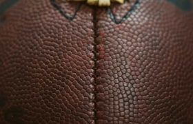 A very close up shot of an American football, featuring its iconic ridge and pigskin brown texture.