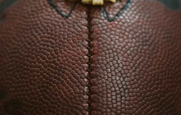 A very close up shot of an American football, featuring its iconic ridge and pigskin brown texture.